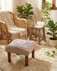 Cozy living room with wicker chairs, a patterned ottoman, and potted plants.
